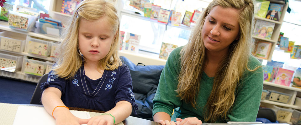 Teacher helping a student with her craft project.