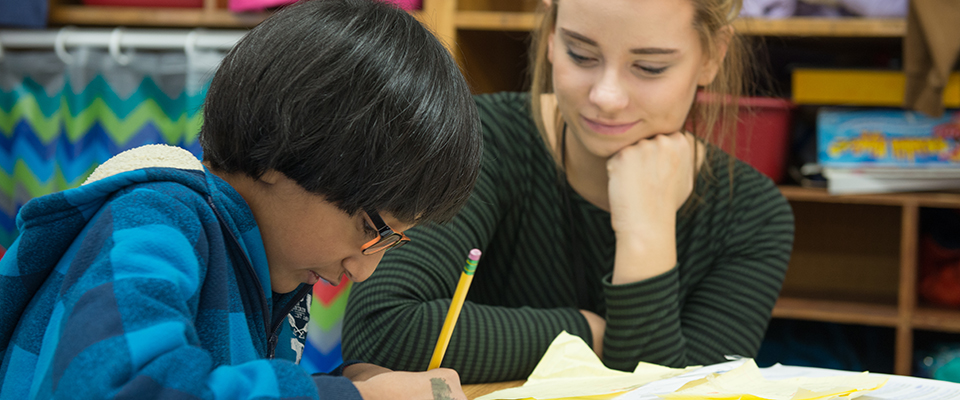 Teacher watching and smiling as a student writes out words.